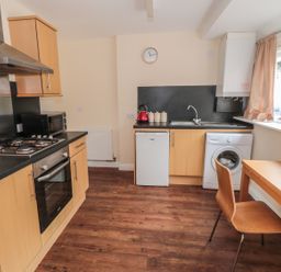 A kitchen with wooden cabinets a gas stove oven microwave small fridge washing machine and a wooden table with a chair at No 1 Low Hall Cottages Scalby near Scarborough