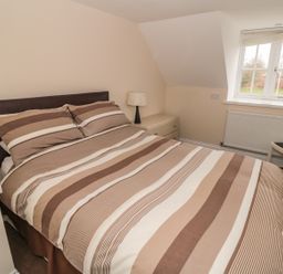 A bedroom with a double bed with striped bedding a bedside table lamp a window and a chair at No 2 Low Hall Cottages Scalby near Scarborough