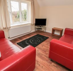 A living room with two red sofas a black rug a television on a glass stand and a wooden side table at No 2 Low Hall Cottages Scalby near Scarborough