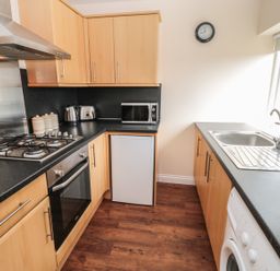 A kitchen with wooden cabinets a gas stove oven microwave kettle toaster small fridge sink and washing machine at No 2 Low Hall Cottages Scalby near Scarborough