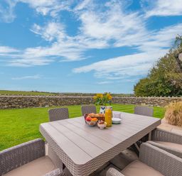 An outdoor patio with a table and chairs set with fruit juice and flowers near a stone wall at Colt Park Cottage in Ulverston