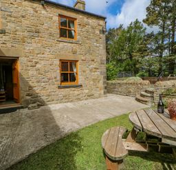 A stone cottage with a wooden door and windows a curved wooden picnic table with plants and a bottle on it in the garden at Moorgair Cottage Slaley near Hexham