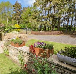 A garden area with flower pots on a stone wall and trees in the background at Moorgair Cottage Slaley near Hexham