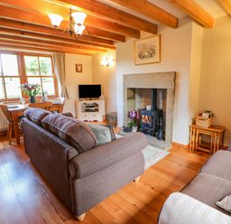 A living room with wooden beams a dining table a fireplace and two sofas at Moorgair Cottage Slaley near Hexham