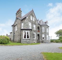 A large stone house with multiple windows and a gravel driveway at Pensarn Hall in Llanbedr near Harlech