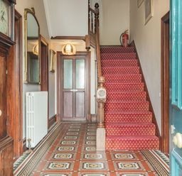 An entrance hallway with a wooden staircase carpeted in red and patterned tile floor at Pensarn Hall in Llanbedr near Harlech