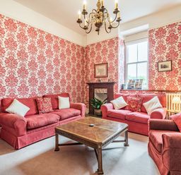 A sitting room with red patterned wallpaper red sofas armchair wooden coffee table and chandelier at Pensarn Hall in Llanbedr near Harlech