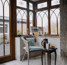 A corner with a wicker chair and cushions next to a small wooden table with a coffee press, cup, and plate of pastries at Stargazer's Field House in Hardwicke near Hay-on-Wye