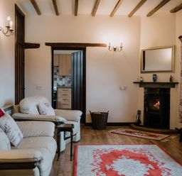 A living room with cream sofas floral cushions a wood burning stove and rugs at Stargazer's Field House Hardwicke near Hay-on-Wye