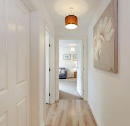 A hallway with wooden floor lamps and flower artwork leading to a living room with a sofa at Perriwinkle The Bay near Filey