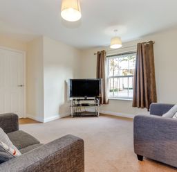 A living room with two sofas a television on a stand and a window with curtains at Perriwinkle The Bay near Filey
