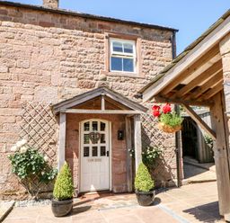The stone exterior of a building with a white door and two potted plants on either side at The Cow Byre in Barras near Kirkby Stephen