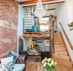 A living area with exposed brick wall wooden stairs chandelier and kitchen at The Cow Byre Barras near Kirkby Stephen