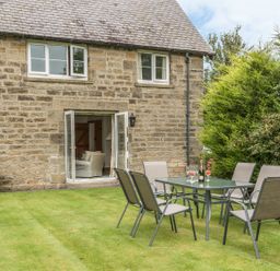A garden with a glass table and six chairs next to a stone house with open doors at Stephen's Cottage in Alnmouth