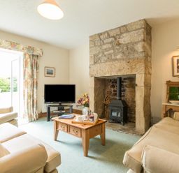 A living room with beige sofas a wooden coffee table a stone fireplace and a television at Stephens Cottage in Alnmouth