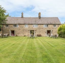 A stone house with open doors and garden chairs and tables on a lawn at Stephens Cottage in Alnmouth