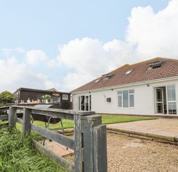 A backyard with a patio table set with glasses and food a charcoal grill and a white house with an open door at On The Watersedge in Beadnell