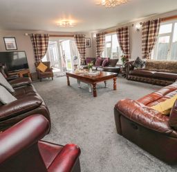 A living room with leather sofas cushions a wooden coffee table and a television at On The Watersedge in Beadnell