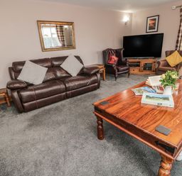 A living room with brown leather sofa armchairs wooden coffee table and a television at On The Watersedge in Beadnell