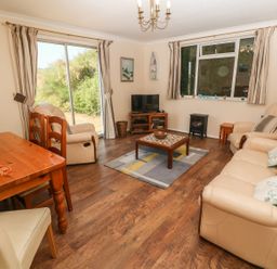 A living room with beige sofas a wooden coffee table a TV on a wooden stand and a dining table at The Shack in Mawgan Porth near Newquay