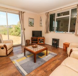 A living room with leather armchairs a wooden coffee table a television and windows with curtains at The Shack in Mawgan Porth near Newquay