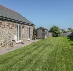 A grass lawn next to a stone wall house with a wooden shed and a fence at Middle Barn in Launceston