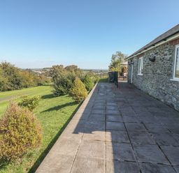 A stone house with a tiled patio and bushes along a grass lawn at Middle Barn in Launceston