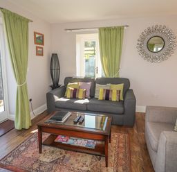 A living room with a gray sofa and armchair a wooden coffee table a decorative mirror and green curtains at Middle Barn in Launceston