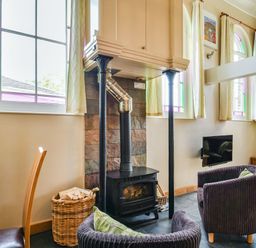 A living room with a wood stove flanked by two black columns and two armchairs near stained glass windows at The New Chapel in Great Hatfield near Hornsea
