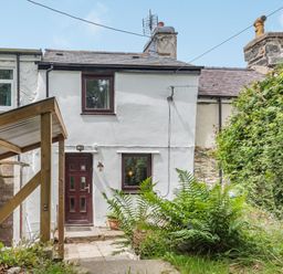 A white two-story house with a brown door and windows a small garden with plants and a covered area with red gas canisters at 3 Tyn Y Mynydd in Penmachno