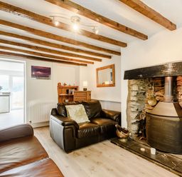 A living room with two leather sofas a stone fireplace wooden beams on the ceiling and a wooden cabinet at 3 Tyn Y Mynydd in Penmachno