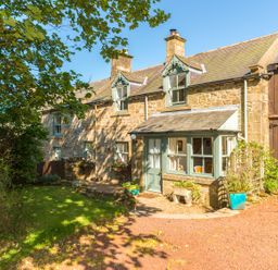Stone cottage with green framed windows and door with plants outside at Townfoot Cottage in Elsdon near Otterburn