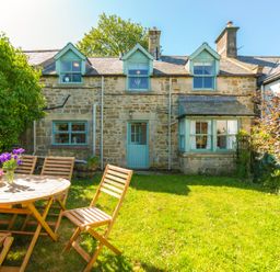 A stone cottage with blue trim windows a blue door and a wooden outdoor table with chairs on grass at Townfoot Cottage Elsdon near Otterburn