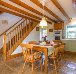 A dining area with a wooden table and chairs set for tea near a staircase and kitchen cabinets at Townfoot Cottage Elsdon near Otterburn