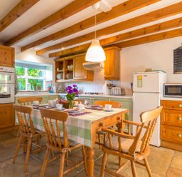 A kitchen with wooden beams a dining table set for breakfast and appliances at Townfoot Cottage Elsdon near Otterburn