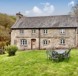 A stone cottage with a wooden door and white windows and a metal outdoor dining table with chairs on grass at The Birches in Hay-on-Wye