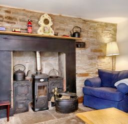 A sitting area with a blue armchair a floor lamp and a fireplace with a wood stove at The Birches in Hay-on-Wye