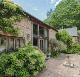 An outdoor view of a stone building with windows and plants at The Lodge Farm Barn in Deepdean near Ross-on-Wye