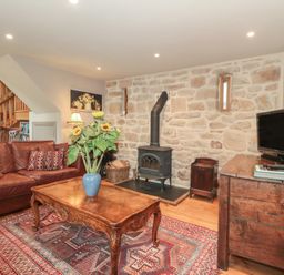 A living room with a sofa, coffee table, and wood stove at The Lodge Farm Barn in Deepdean near Ross-on-Wye