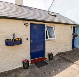 The exterior of a stone building with a blue door and flower pots at Ffynnon Tom in Trefin near St Davids