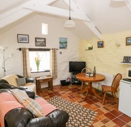 A living room with leather sofas a wooden round table a television and kitchen appliances at Ffynnon Tom in Trefin near St Davids