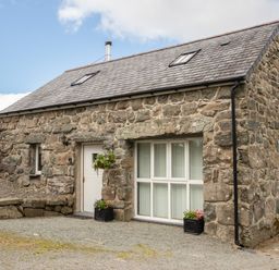 A stone cottage with a white door and window with flower pots outside at Hendre Cottage Bronaber near Trawsfynydd