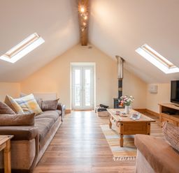 An attic living room with a sofa a coffee table a wood burner TV and skylight windows at Hendre Cottage Bronaber near Trawsfynydd