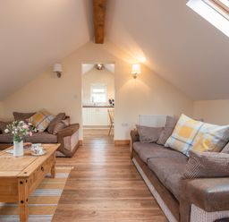 A living room with two brown sofas a wooden coffee table with flowers and cups and a view to a kitchen at Hendre Cottage in Bronaber near Trawsfynydd