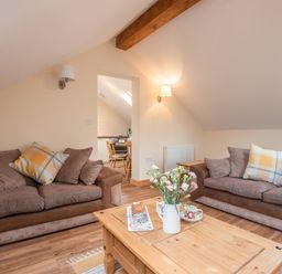 A living room with two brown sofas and a wooden coffee table with flowers and cups at Hendre Cottage Bronaber near Trawsfynydd