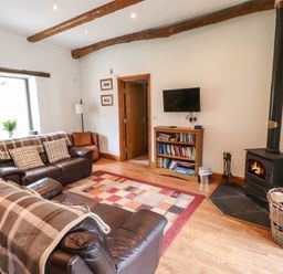 A living room with two leather sofas a wood burning stove and a bookshelf at The Hayloft in Newlands near Braithwaite and Keswick