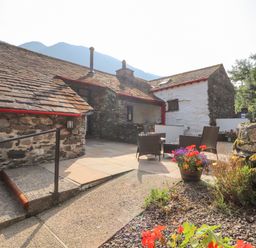An outdoor patio area with stone walls and slate roof a seating area with chairs and a table flower pots with colorful flowers and a stone pathway at The Hayloft in Newlands near Braithwaite and Keswick