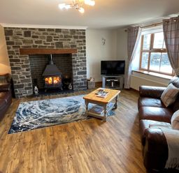 A living room with a stone fireplace wood burner two leather sofas a wooden coffee table a television and window with curtains at Tangaer Cottage in Cellan near Lampeter