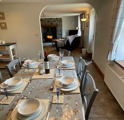 A dining table set with plates glasses and a bottle of wine near a living room with a wood stove at Tangaer Cottage in Cellan near Lampeter