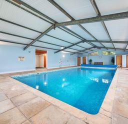 An indoor swimming pool with blue water surrounded by tiled floor and seating areas at Old Rectory Cottages Aberhafesp near Newtown
